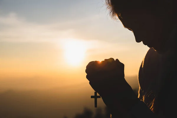 Silhouette of young  human hands praying with a  cross at sunris — Stock Photo, Image