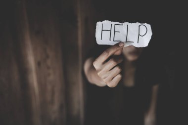 Depresif bir ifadeyle yalnız oturan ve yardım mesajıyla kağıt gösteren kadınlar. Kadınlara yönelik şiddeti durdurun.