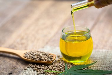 Bulanık arka planda cam bir kavanoza kenevir yağı dökülüyor..