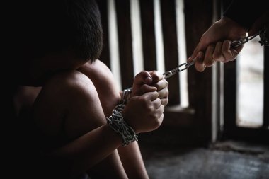 Bileğinde zincirle yerde oturan tacizci çocuk, insan hakları ihlali, insan kaçakçılığı. Boşluğu Kopyala 