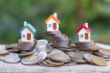 Beyaz arka planda madeni para yığını, yatırım riski kavramı ve emlak piyasasındaki belirsizlik üzerine mini ev. 