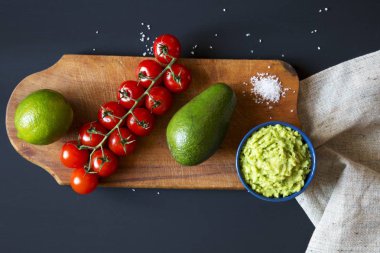 Geleneksel neşeli Meksika sosu guacamole seramik kase ve malzemelerin üzerine eski kesme tahtası. Koyu arka plan. Üstten Görünüm. Düz yatıyordu. 