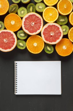 Düz yatıyordu. Üstten Görünüm. Dilimlenmiş renkli taze meyve ile ahşap tahta: kivi, portakal, greyfurt ve mandarin. Hindistancevizi, kireç ve avokado. Siyah arka plan. Yaz arka plan.