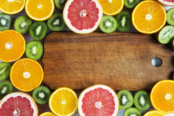 Plat lag bovenaanzicht houten plank met gesneden kiwi, sinaasappel, grapefruit en Mandarijn op lichte achtergrond. Zomer achtergrond — Stockfoto