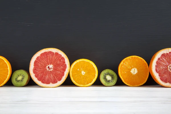 Gesneden kiwi, sinaasappel, grapefruit en een Mandarijn op zwart-wit houten achtergrond. Kopieer ruimte. Zomer achtergrond — Stockfoto
