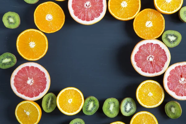 Deitado. Vista superior. Placa de madeira com frutas frescas coloridas fatiadas: kiwi, laranja, toranja e tangerina. Cocos, lima e abacate. Fundo preto. Fundo de verão . — Fotografia de Stock