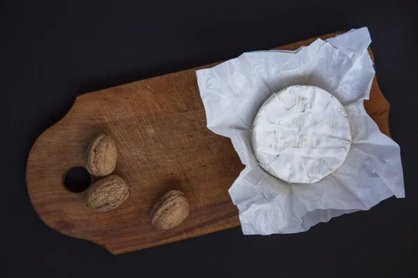 Sýr camembert nebo brie na tmavé dřevěné desce s oříšky. Tmavé pozadí. Produkce mléka. Byt leží. Z výše uvedeného. Pohled shora. — Stock fotografie