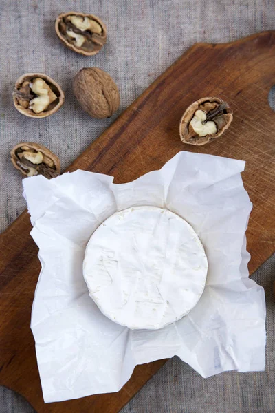 Ronde Camembert kaas of brie in papier met walnoten op het bord. Bekijk van bovenaf. Van bovenaf. Verouderde textuur van jute. Plat leggen. — Stockfoto