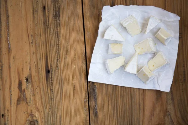 Trozos de queso redondo brie o camembert en papel sobre fondo de madera. Vista superior. Desde arriba . —  Fotos de Stock