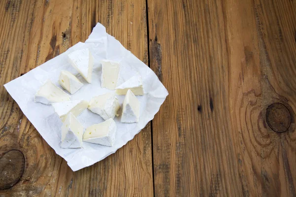 Trozos de queso redondo brie o camembert en papel sobre fondo de madera. Vista lateral. Copiar texto . —  Fotos de Stock