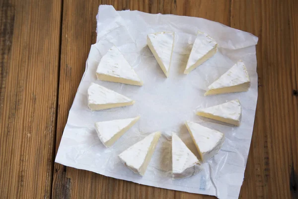 Trozos de queso redondo brie o camembert en papel sobre fondo de madera . —  Fotos de Stock