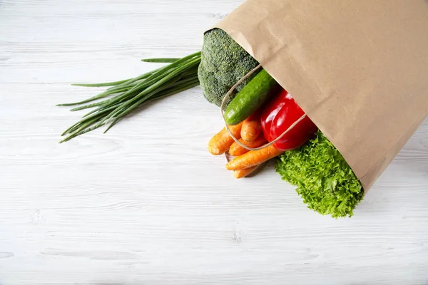 Paper bag of different vegetables on wooden background. Healthy food. Top view. From above. Copy space.