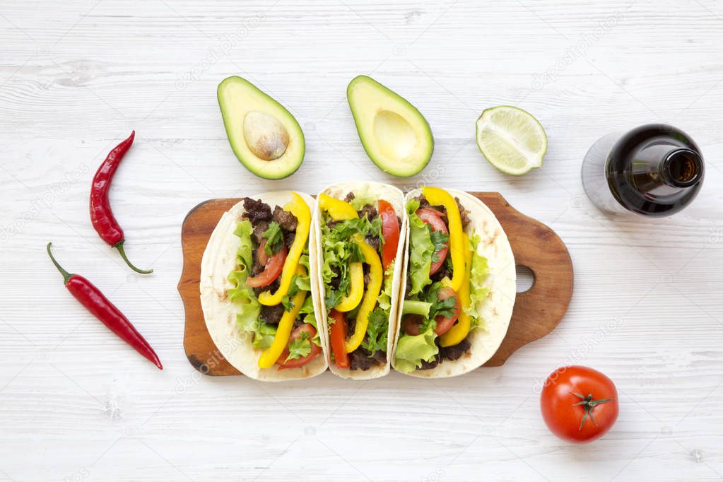 Tacos with pork, vegetables, avocado,lime and beer. Mexican kitchen. White wooden background. Top view, flat, overhead. 