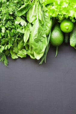 Yeşil sebze ve meyve üzerinde koyu renk arka plan (avokado, kireç, lahana, maydanoz, salatalık, dereotu, soğan, salata, ıspanak). Uzay kopyalayın. Yan görünüm.