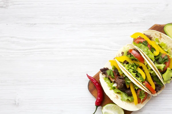 Tacos mit Schweinefleisch, frischem Gemüse, Avocado, Limette und Pfeffer. weißer Holzhintergrund. Draufsicht, flach, über Kopf. Kopierraum. — Stockfoto