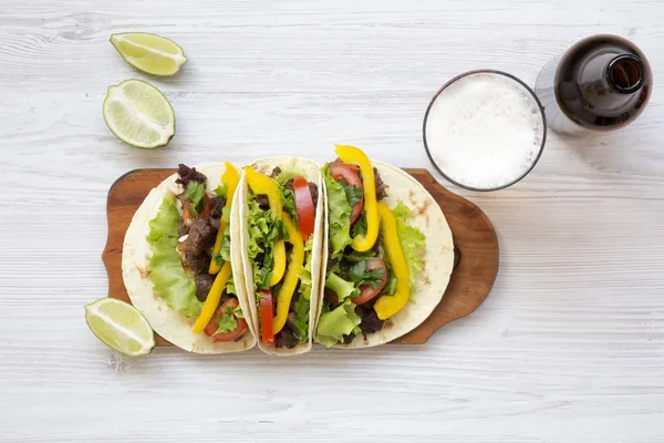 Tacos con carne di maiale, verdure, avocado, lime e birra. Cucina messicana. Fondo in legno bianco. Vista dall'alto, pianeggiante, sopraelevata . — Foto Stock