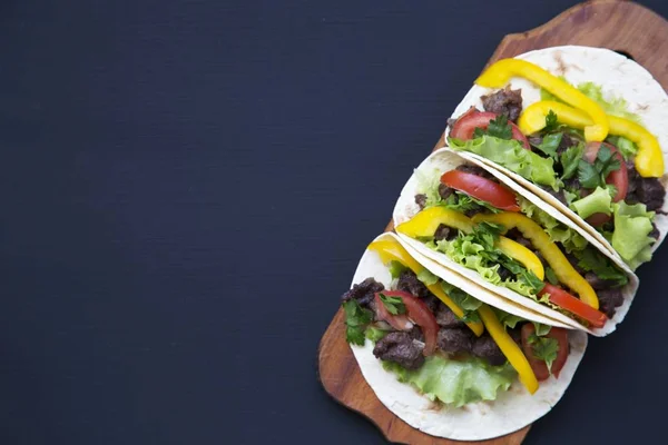 Tacos con carne e verdure sul bordo su uno sfondo di legno nero, vista dall'alto. Sfondo nero per testo e design. Vista dall'alto piatta . — Foto Stock