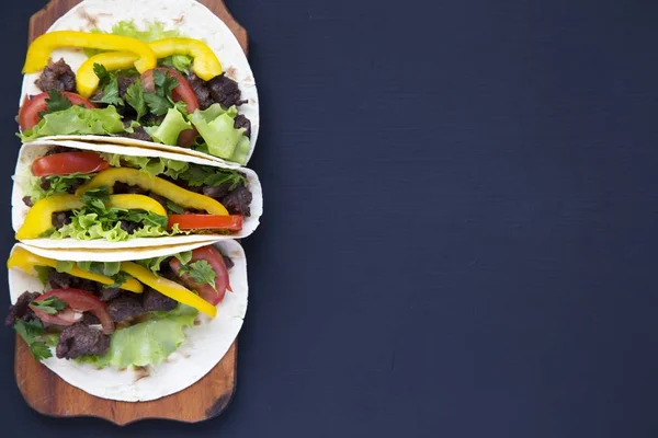 Tacos con carne e verdure sul bordo su uno sfondo di legno nero, vista dall'alto. Sfondo nero per testo e design. Vista dall'alto piatta . — Foto Stock