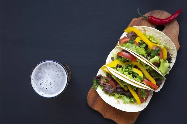 Tacos con birra sul bordo su uno sfondo di legno nero, vista dall'alto. Sfondo nero per testo e design. Vista dall'alto piatta . — Foto Stock