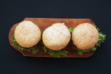 Ahşap tahta üzerinde taze Amerikan burger. Koyu arka plan. Üstten Görünüm. Yukarıdan.