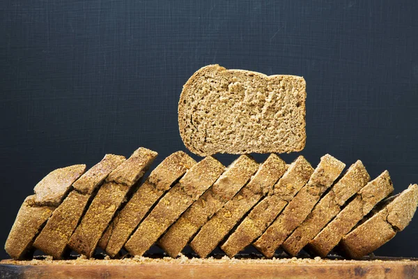 Sliced bread on wooden board. Dark background. Side view. — Stock Photo, Image