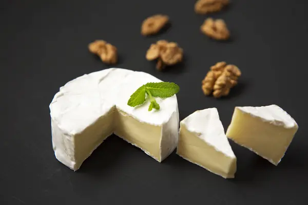 Sýr camembert nebo brie s vlašským ořechem na tmavém pozadí. Boční pohled. — Stock fotografie
