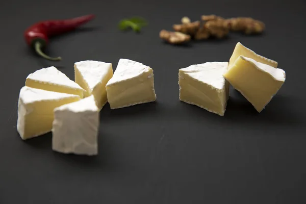 Slices of cheese camembert or brie  with walnuts and chili pepper. Milk production. Side view. — Stock Photo, Image