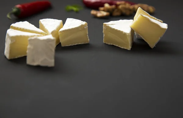Slices of cheese camembert or brie  with walnuts and chili pepper. Milk production. Side view. — Stock Photo, Image