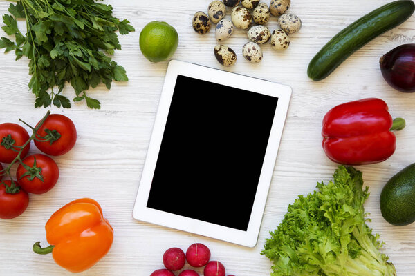Healthy food concept. Raw fruits and vegetables wirh tablet on a white wooden background. Flat lay. Top view. From above.