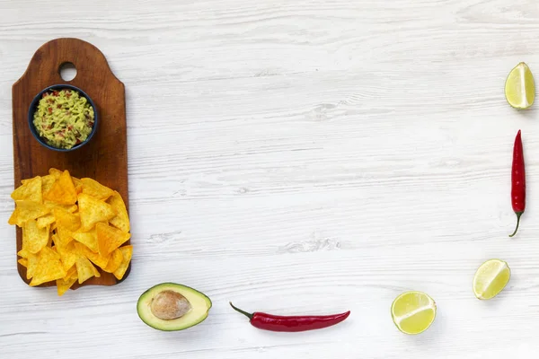 Kom van traditionele Mexicaanse guacamole en ingrediënten met nachos op houten bord. Witte houten achtergrond. Bovenaanzicht. — Stockfoto