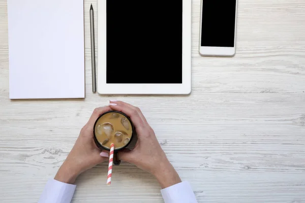 Γυναίκα κατέχει ένα φλυτζάνι του latte πάγου. Γυναικείας εργασίας με latte πάγου, tablet, smartphone και σημειωματάριο. Αντιγράψτε το χώρο. Το Top view. Από πάνω. — Φωτογραφία Αρχείου