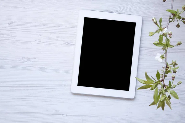 Ahşap masa çiçek açması kiraz dal üstten görünüm ile dekore edilmiş bir beyaz üzerine tablet