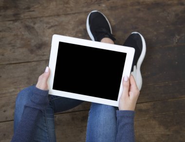 Kız bir ahşap zemin üzerinde oturur ve bir tablet boş bir ekran ile onun elinde tutar. Üstten Görünüm.