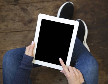 Kız bir ahşap zemin üzerinde oturur ve bir tablet ile izole perde onun elinde tutar. Üstten Görünüm.