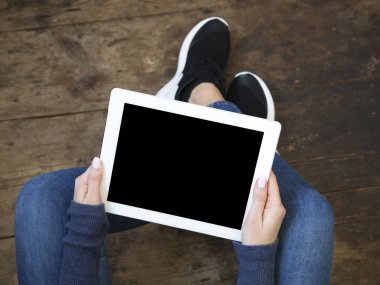 Kız bir ahşap zemin üzerinde oturur ve bir tablet ile izole perde onun elinde tutar. Üstten Görünüm.