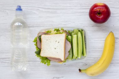 Sağlıklı okul öğle yemeği kutusu taze organik sebze sandviç, meyve ve şişe su beyaz ahşap zemin üzerinde düz yatıyordu. Yukarıdan.