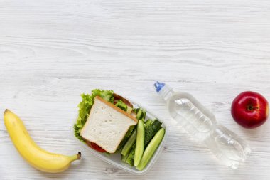 Üstten Görünüm okul öğle yemeği kutusu sandviç, meyve ve şişe su beyaz ahşap zemin üzerinde düz yatıyordu. Yukarıdan. Kopya alanı.