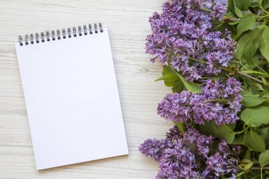 Beyaz ahşap zemin üzerinde defter ile Lila çiçek bir buket. Uzay kopyalayın. Anneler günü. Yukarıdan, lay düz.
