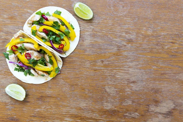 Tacos with grilled chicken fillet, fresh vegetables, lime on rustic wooden background. Top view, from above. Copy space.