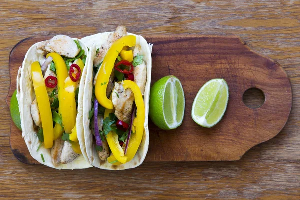 Tacos with grilled chicken fillet, fresh vegetables, lime on wooden board. Top view, from above. Flat lay.