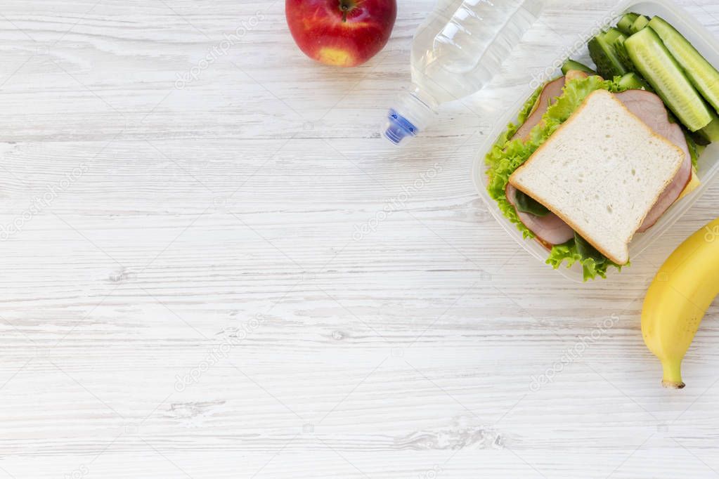 Healthy school lunch box with sandwich, fruits and bottle of water on white wooden background, flat lay. From above. Copy space.