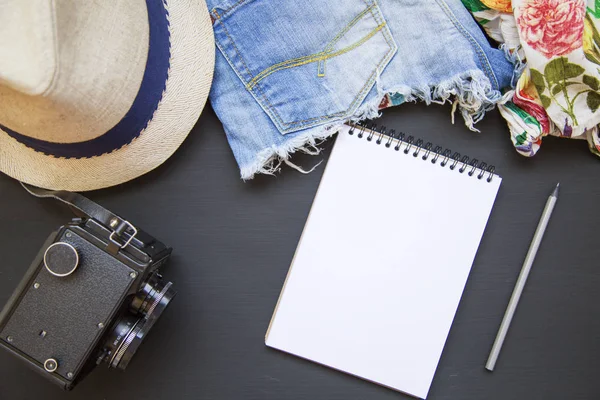 Summer set of women's clothes. Female blouse with denim shorts, hat, vintage camera and notebook. Top view. From above. — Stock Photo, Image