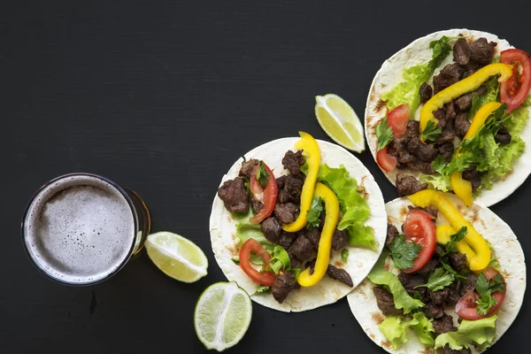 Gustosi tacos con carne e verdure, birra e lime su sfondo nero, vista dall'alto. Cucina messicana. Ricevuto. Posa piatta . — Foto Stock