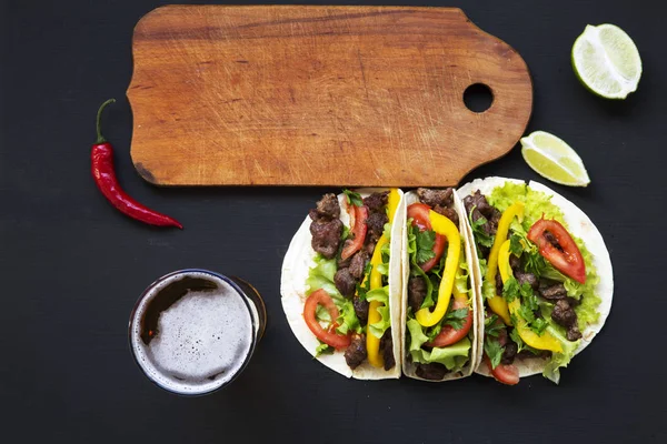 Tacos with beef and vegetables, beer and lime on a black background, top view. Mexican kitchen. Copy space. Flat lay. — Stock Photo, Image