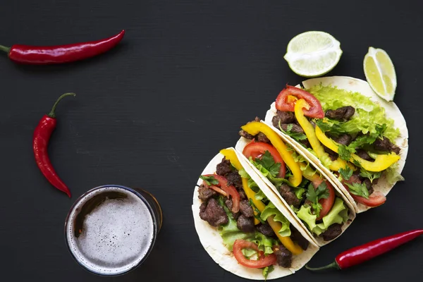 Tacos mexicanos con carne de res y verduras, cerveza y lima sobre fondo negro, vista superior. Copiar espacio . — Foto de Stock