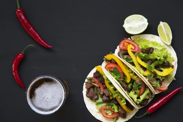 Tacos con carne de res y verduras, cerveza y lima sobre fondo negro, vista superior. Cocina mexicana. Copiar espacio . —  Fotos de Stock