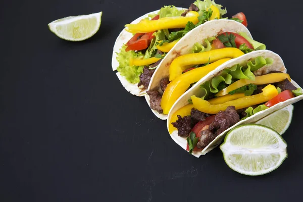 Tacos mit Rindfleisch und Gemüse und Limette auf schwarzem Hintergrund, Seitenansicht. Nahaufnahme. — Stockfoto