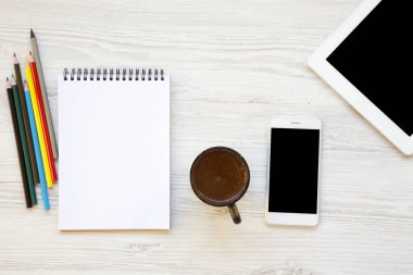 Çalışma alanı ile akıllı telefon, defter, renkli kalemler, tablet ve latte Beyaz ahşap zemin üzerinde. Yukarıdan.