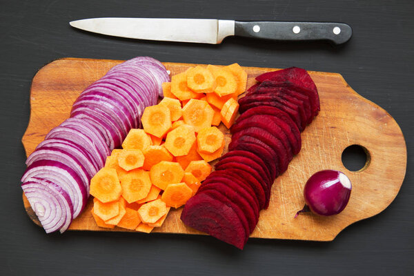 Нарезанные свежие овощи на деревянной доске на темном фоне. Вид сверху
. 