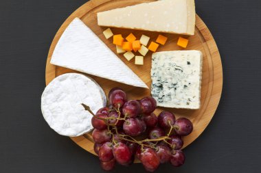 Koyu arka plan üzerinde yuvarlak ahşap tahta üzerinde üzüm ile farklı peynir kümesi. Romantik yemek. Düz yatıyordu. Yukarıdan, ana sayfa görünümü.